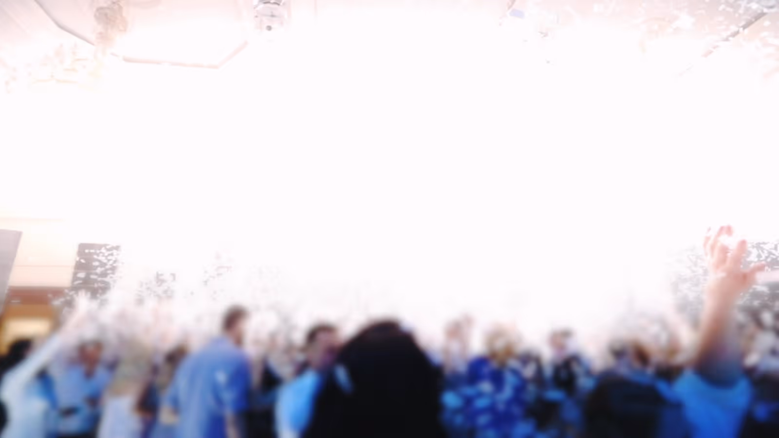 Blurred crowd dancing with raised arms in bright light as confetti falls