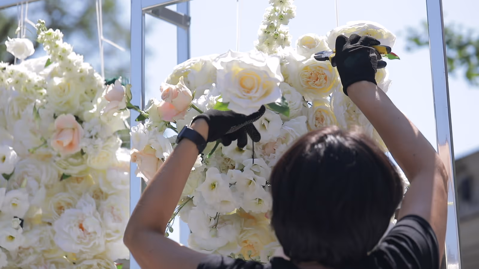 Mains gantées disposant une composition foisonnante de roses blanches et rosées sur une structure extérieure.