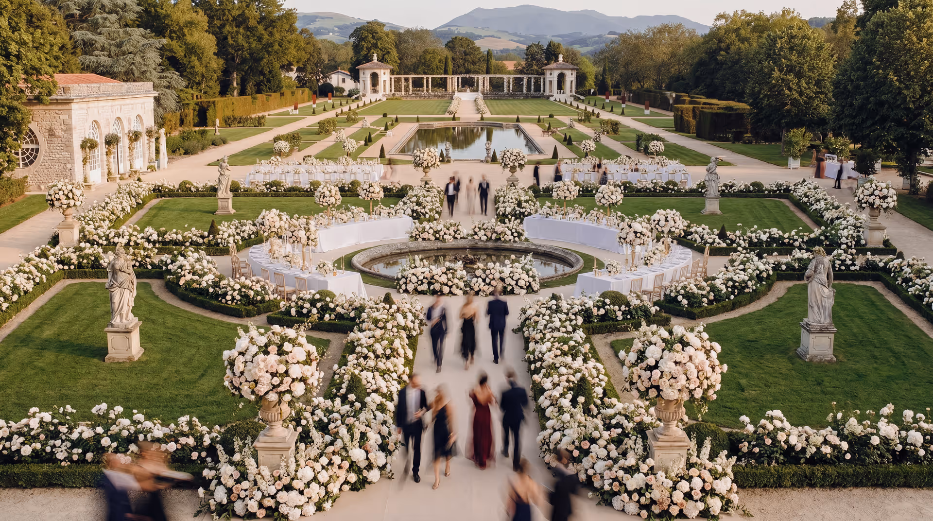 Vue aérienne d'un jardin à la française dressé pour une réception de mariage de luxe, parterres bordés de roses, statues et bassins