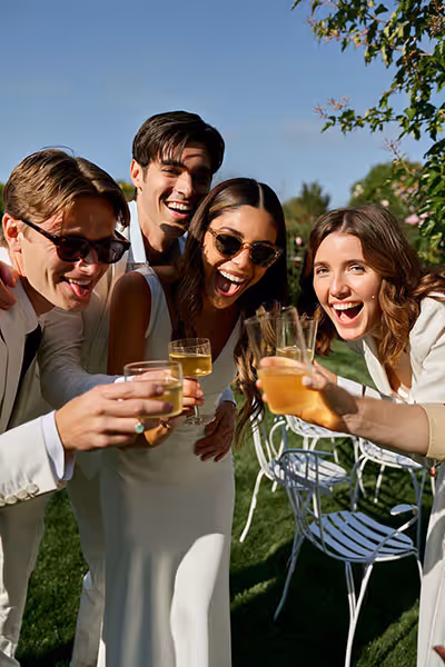 Amis trinquant dans un jardin ensoleillé lors d'une réception de mariage en France