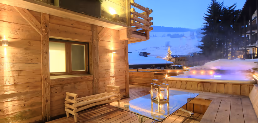 Chalet terrace with outdoor jacuzzi, lanterns and snow-covered mountains at dusk, Megève
