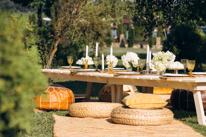 Low garden table with candles, hydrangeas, amber glasses and woven poufs on the grass